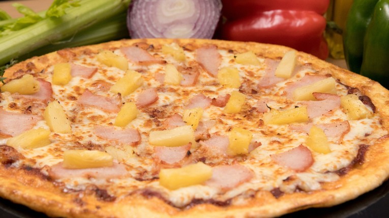 eine große Runde Pizza Hawaii mit Ananas, Schinken und Käse als Belag