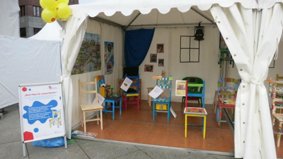 Foto von einem Zelt, in dem bemalte Stühle stehen. Die Stühle sind kreativ zu Kinderrechten gestaltet.