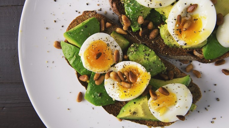 Zwei Brotscheiben auf Teller, belegt mit Avocadoscheiben und geschnittenem Ei.