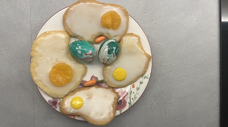 Vier Kekse liegen auf einem Teller in der Mitte des tellers sind zwei bemalte Eier und zwei Mini Deko Möhren.