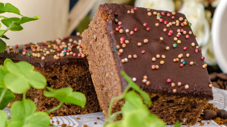zwei kleine, quadratische Schokoladen-Blechkuchenstücke mit Streuseln sind zu sehen. Links im Vordergrundund mittig sind Kleeblätter zu sehen