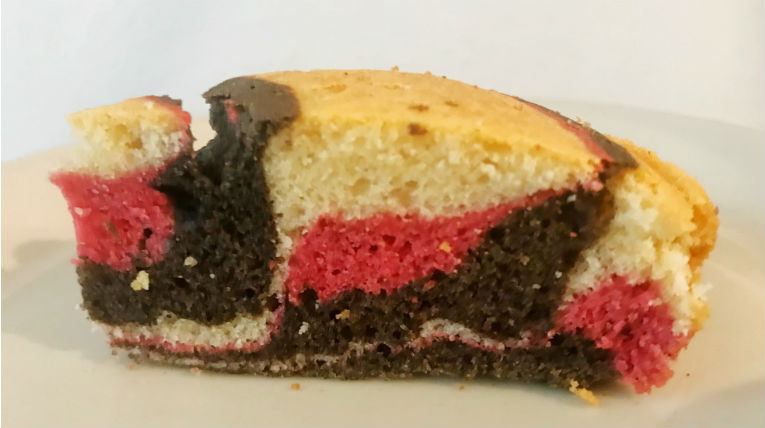 ein Stück heller Rührkuchen auf einem hellen Keramikteller, der Kuchen ist mit Lebensmittelfarbe schwarz, rot und gelb eingefärbt