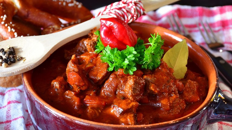 Eine Schüssel gefüllt mit Gulasch. Also Fleisch in viereckigen Stücken, in rot brauner Soße. 