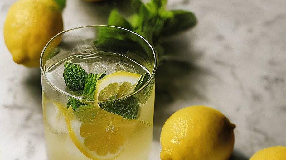 Zitronenlimonade im Glas mit Zitronenscheiben, Minzblättern und Eiswürfeln