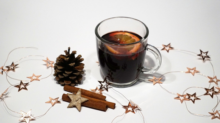 Punsch in Glastasse mit Orangenscheibe garniert, Tannenzapfen und Zimtstangen links neben der Tasse, Sternengirlande als Deko 