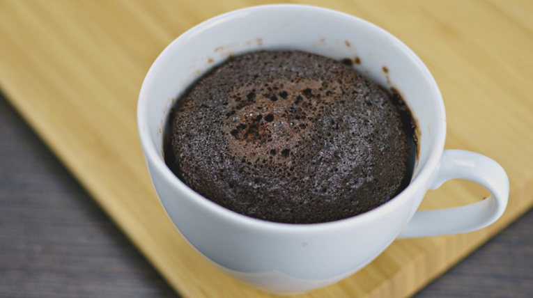 Brownie in Tasse gebacken; weiße Tasse steht auf Holzbrett
