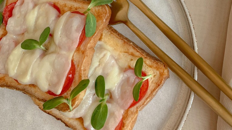 Zwei Toastscheiben, die mit Käse und Tomate überbacken sind.
