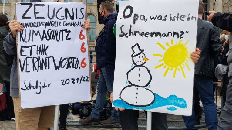 Zwei Demoplakate mit Zeugnis für die Klimapolitik und der Frage, was ein Schneemann ist