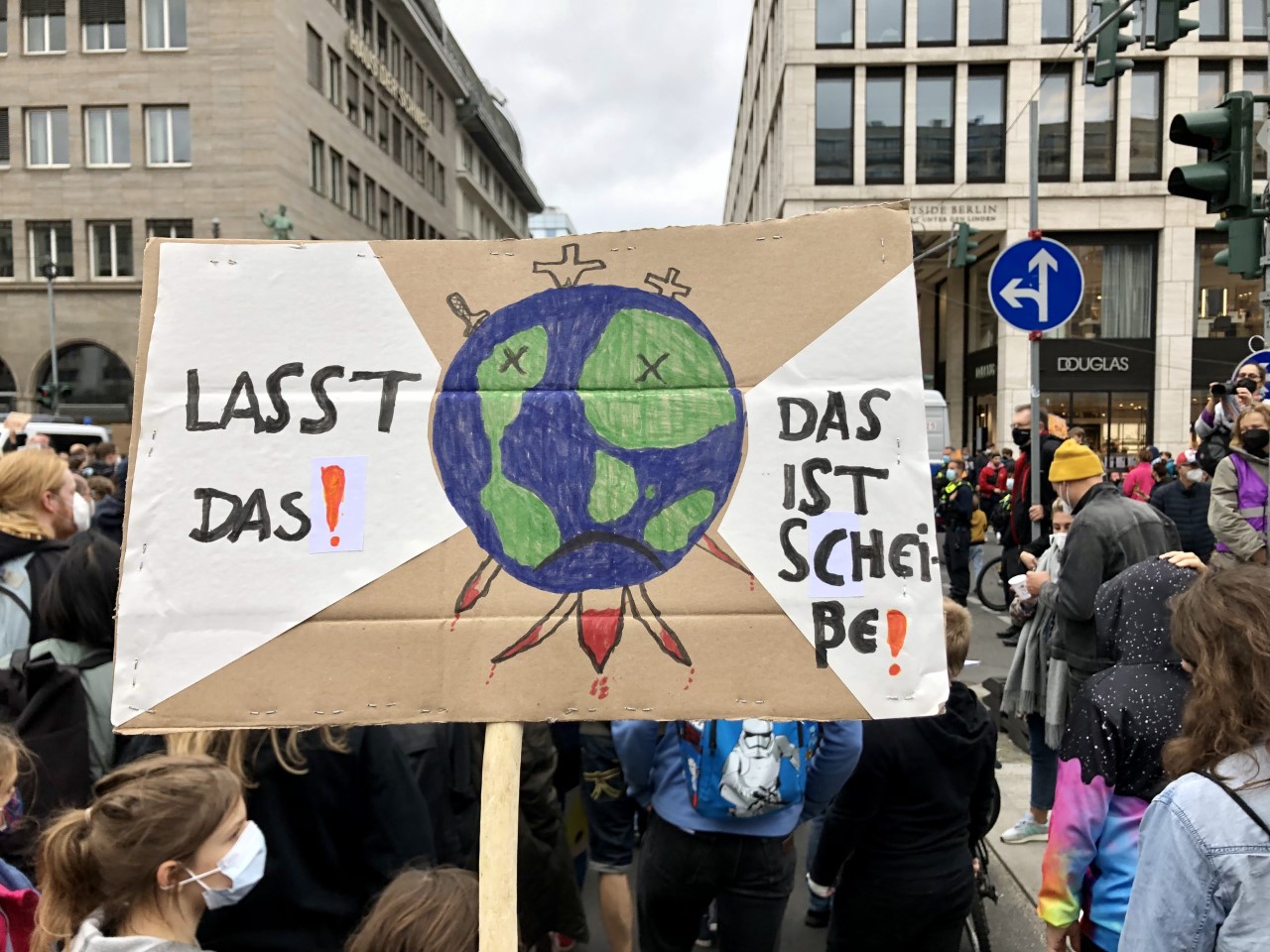 selbstgebasteltes Demoplakat mit Weltkugel von blutigen Dolchen durchstoßen und der Aufschrift Lasst Das! Das ist Scheiße!