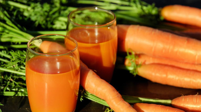 Orangener Saft in Gläsern, im Hintergrund liegen Karotten mit Möhrengrün