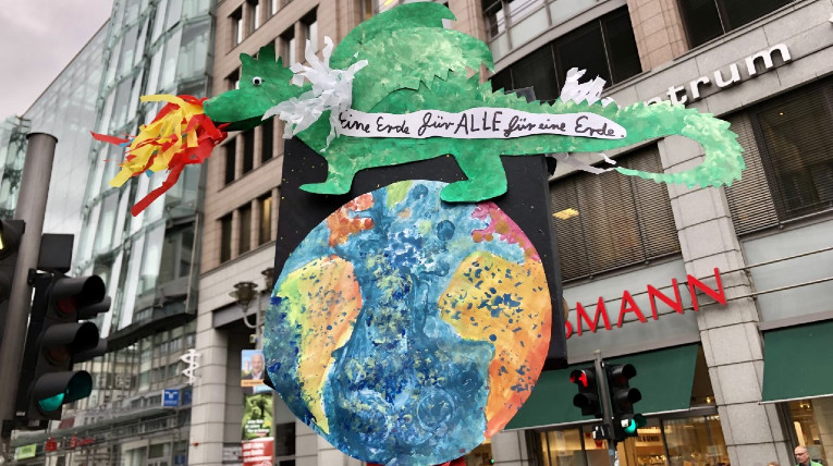 selbstgebasteltes Demoplakat, ein feuerspeiender Drache sitzt auf der Weltkugel, mit der Aufschrift Eine Erde für ALLE für eine Erde!