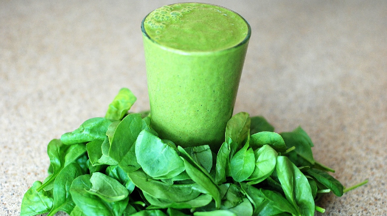 Grüner Smoothie im Glas, steht in einem Bett aus Spinatblättern