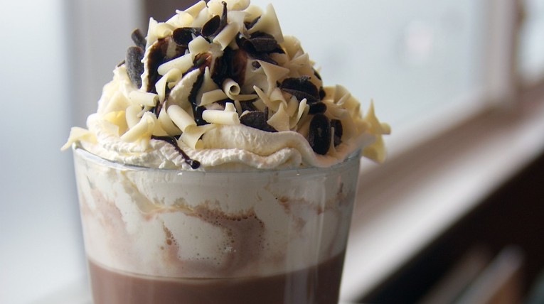 Ein großes Glas mit heißer Schokolade - Milch und Kakao. Oben drauf ist Sahne und Schokoraspeln