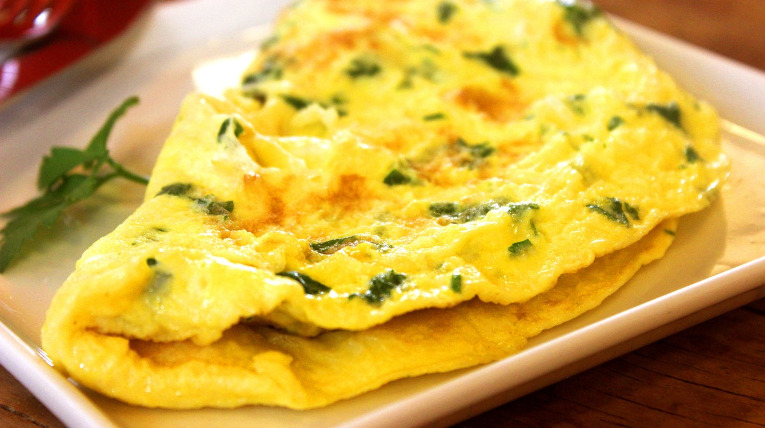 Omelette umgeklappt auf einem Teller, serviert mit Kräutern
