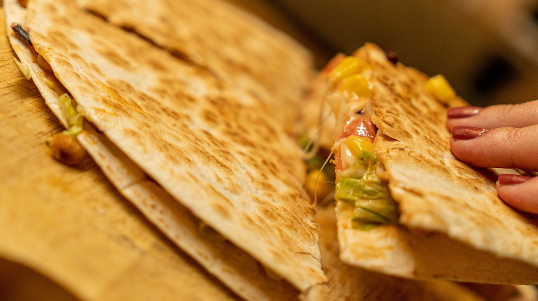 Eine Hand nimmt ein Viertel eines runden Quesadillas. Darin ist geschmolzener Käse und Gemüse.
