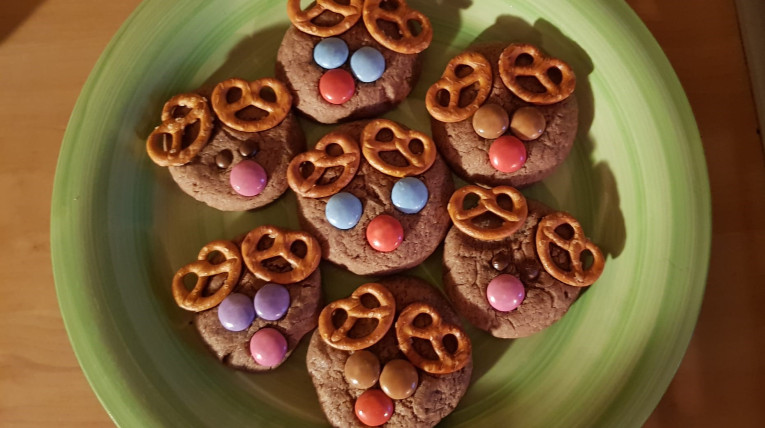 Selbstgebackene Schoko-Kekse; verziert mit jeweils zwei kleinen Salzbrezeln als Geweih und bunten Smarties als Augen und Nase 