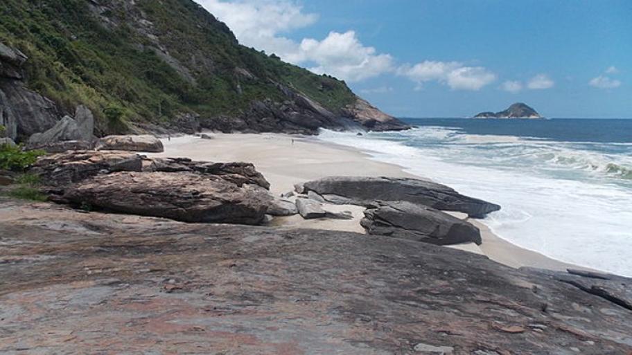 Meeresküste mit Strand, dahinter graue Felsen