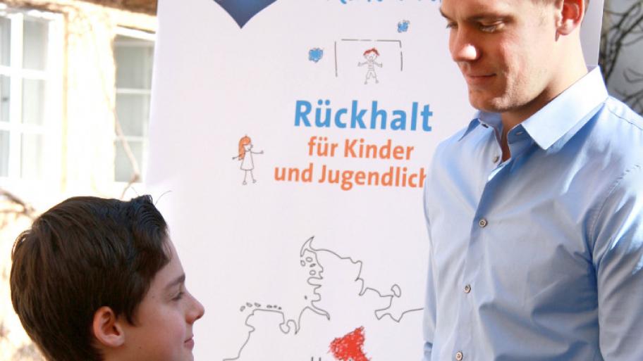 Manuel Neuer und ein Junge vor einem Aufsteller von Manuel Neuers Kinder-Foundation Manus