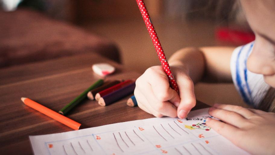 ein Kind füllt mit bunten Farben ein Arbeitsblatt in der Schule aus
