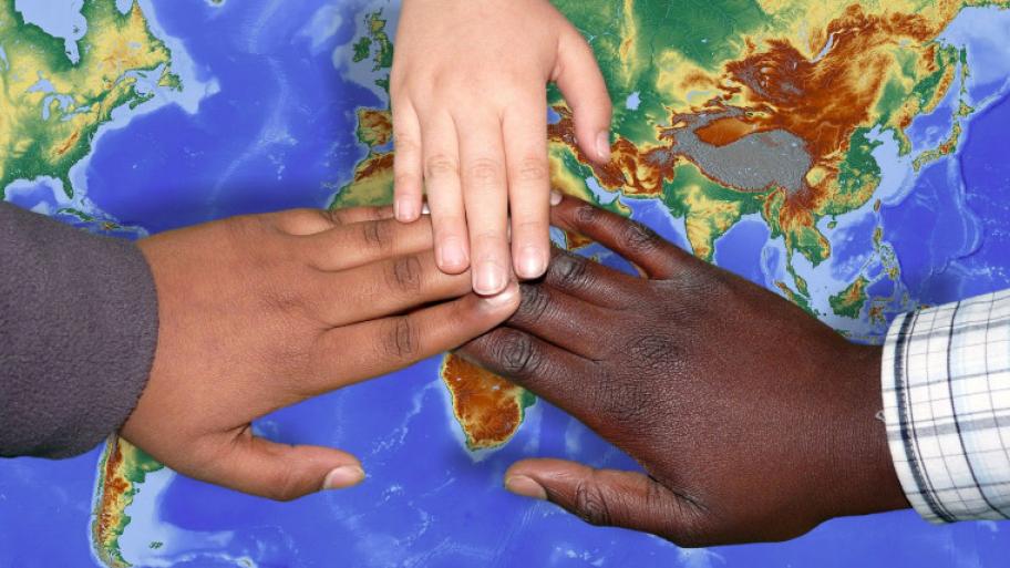 3 Kinderhände unterschiedlicher Hautfarbe liegen auf einer Weltkarte, die Fingerspitzen berühren sich