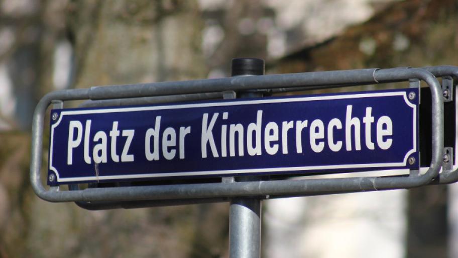 blaues Straßenschild mit weißer Schrift, zu lesen ist "Platz der Kinderrechte"