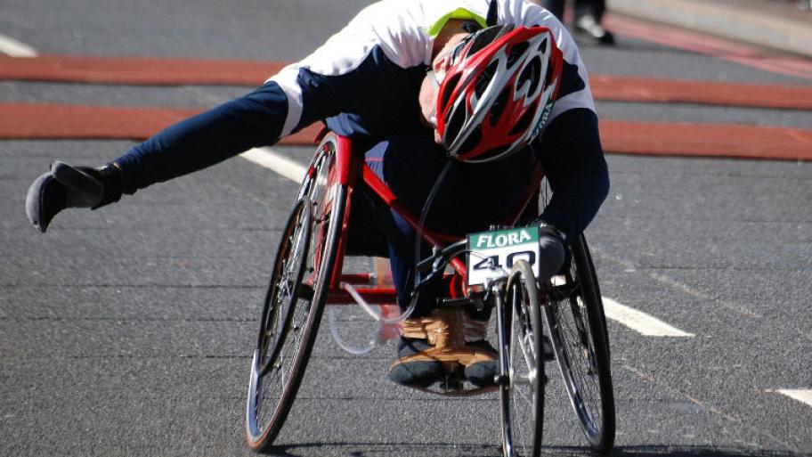 ein Rollstuhlrennfahrer fährt in seinem Rollstuhl mit Sportkleidung und Helm sitzend ein Rennen