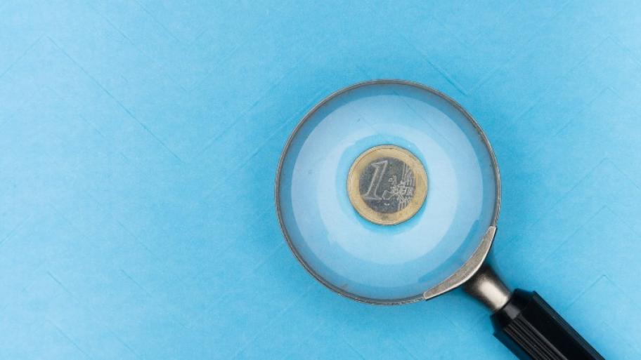 eine Ein-Euro-Münze liegt auf hellblauer Unterlage und wird durch eine Lupe mit schwarzem Griff vergrößert