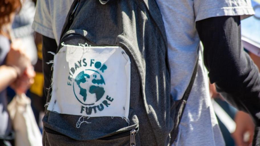 jugendliche*r von hinten, Kopf abgeschnitten, trägt einen blauen Rucksack, darauf ein Aufnäher mit Weltkugel und Schriftzug "Fridays for future"