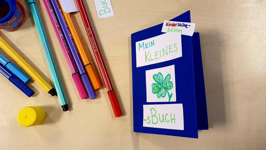 Ein dunkelblaues Minibuch mit der Aufschrift "Mein kleines Glücksbuch". Die Schrift ist grün und ein vierblättriges Kleeblatt ist drauf gemalt.