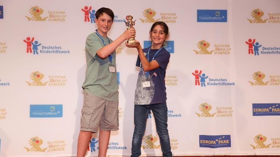 zwei Preisträger vom Deutschen Kinder- und Jugendpreis 2022 halten gemeinsam ihren Preis in die Luft