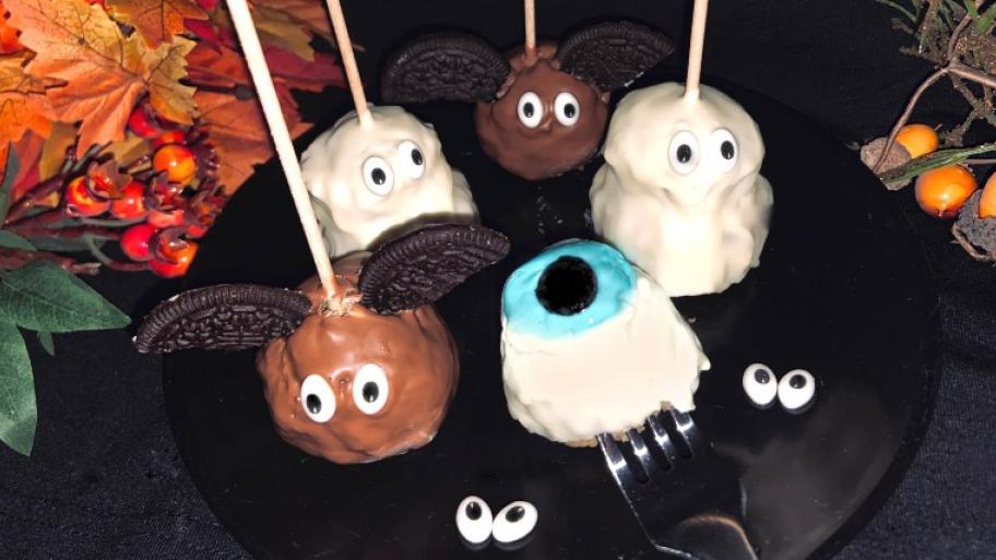 auf einem schwarzen Teller auf Schaschlik-Spieße aufgespießte Cakepops mit heller und dunkler Schokolade überzogen und mit Zuckeraugen