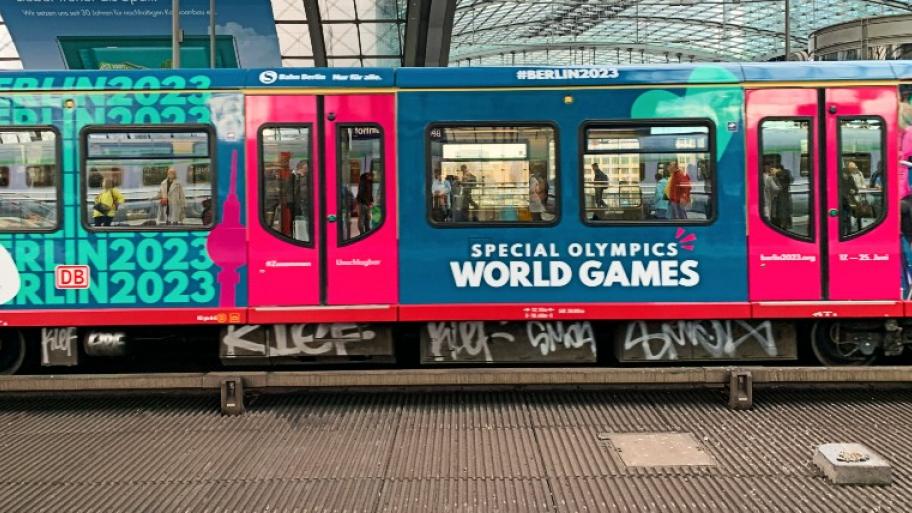 eine S-Bahn steht im Hauptbahnhof in Berlin am Bahnsteig, die Waggons sind rosa und türkis, darauf Werbung für die Special Olympics World Games 2023 in Berlin