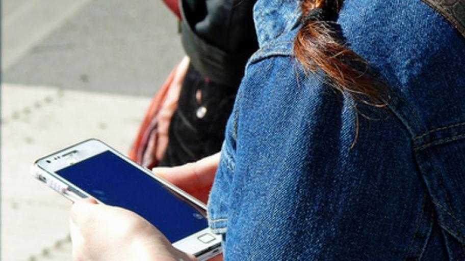 ein Kind von hinten in blauer Jeansjacke, es hält sein Handy in den Händen