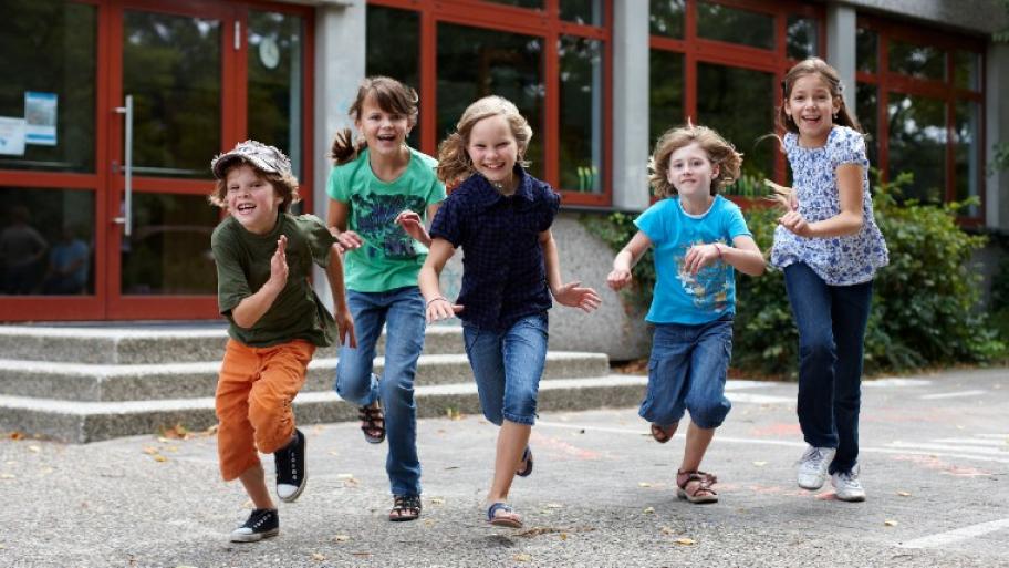 Fünf fröhliche Kinder rennen auf dem Schulhof 