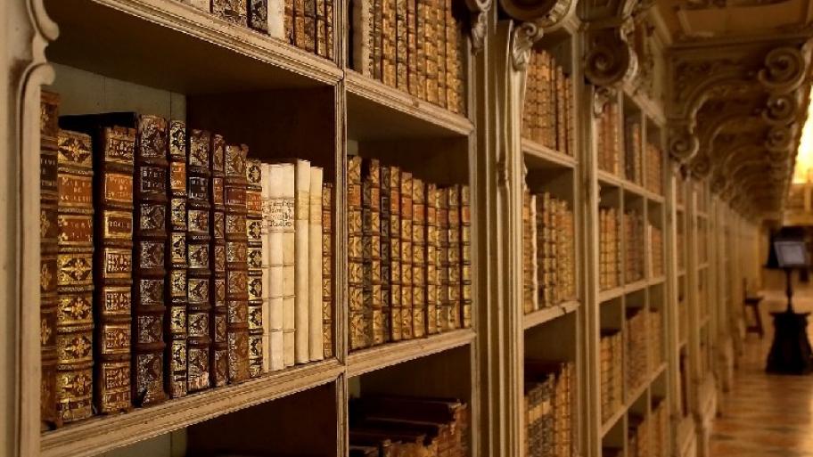 Zu sehen ist ein Bücherregal, in welchem viele alter Bücher mit goldverzierten Bücherrücken stehen. 