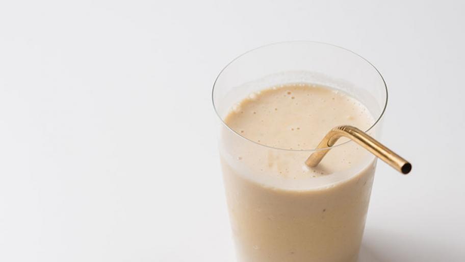 Bananenmilch in einem Glas mit goldenem Strohalm aus Aluminium, Hintergrund weiß