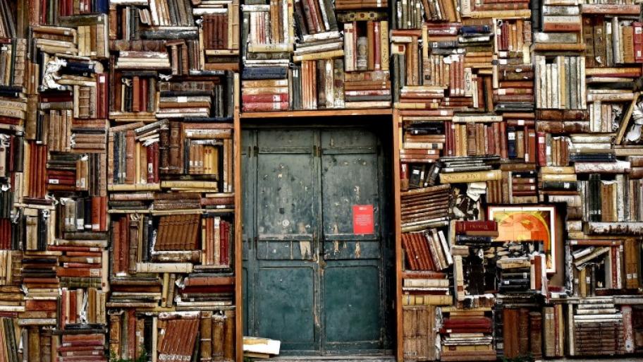 Bücherregale, in denen die Bücher kreuz und quer übereinander gestapelt liegen, in der Mitte eine Tür