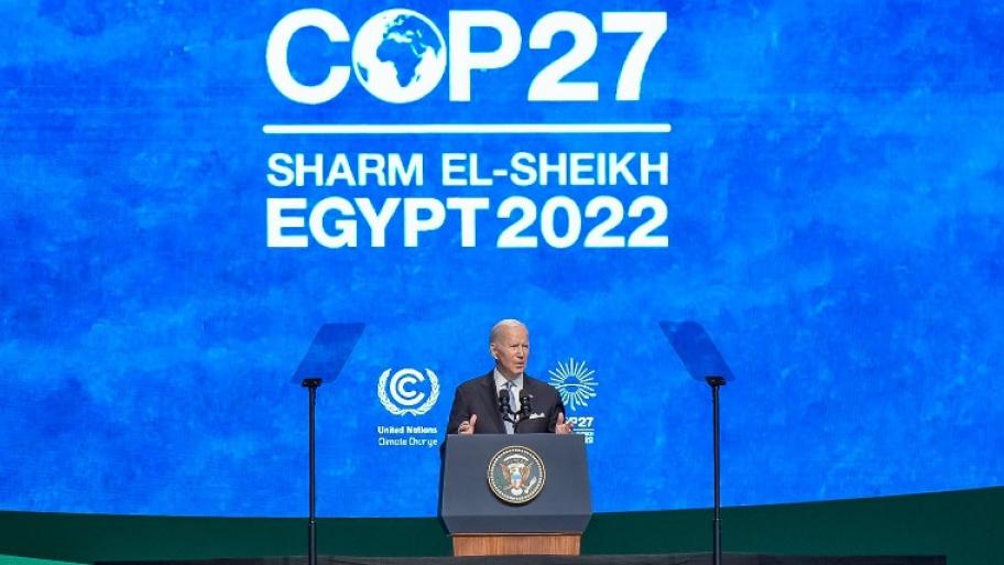 Joe Biden spricht auf Bühne in ein Mikrofon. Dahinter ist groß das Logo der Klimakonferenz zu sehen  