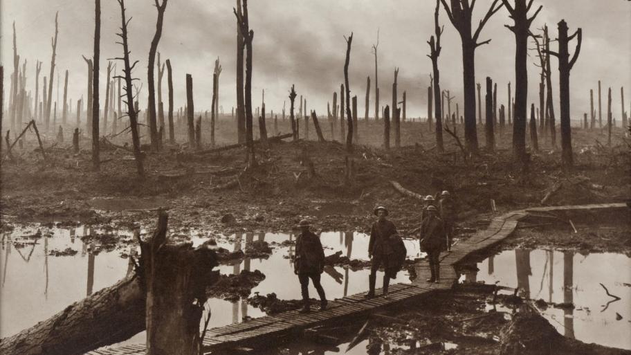 eine Handvoll Soldaten während des 1. Weltkrieges läuft über einen hölzernen Steg, dahinter zerstört Landschaft mit aufragenden Baumstümpfen