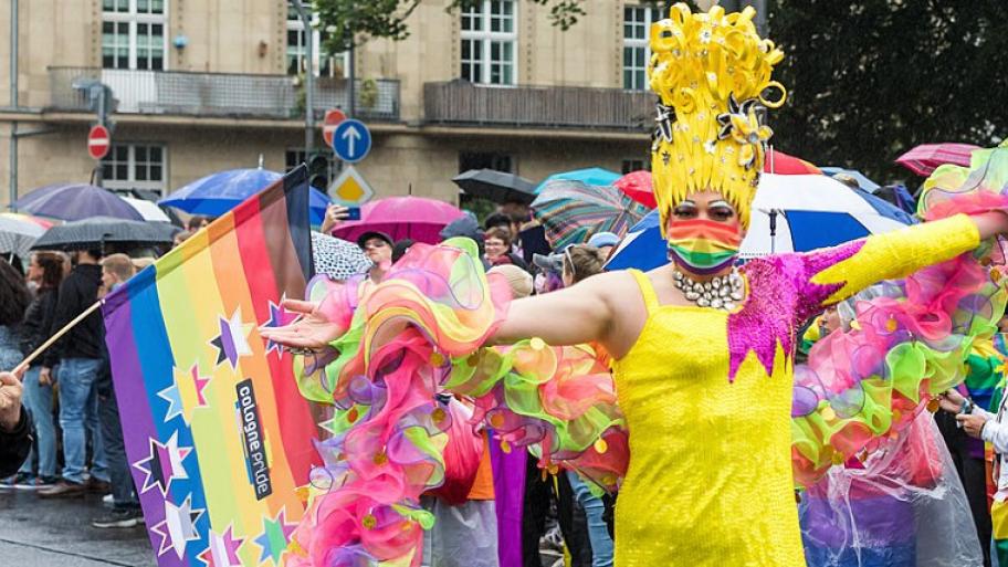 Pride in Köln, Regenbogenflagge und kostümierte Person mit Kopfschmuck und Regenbogen-Maske