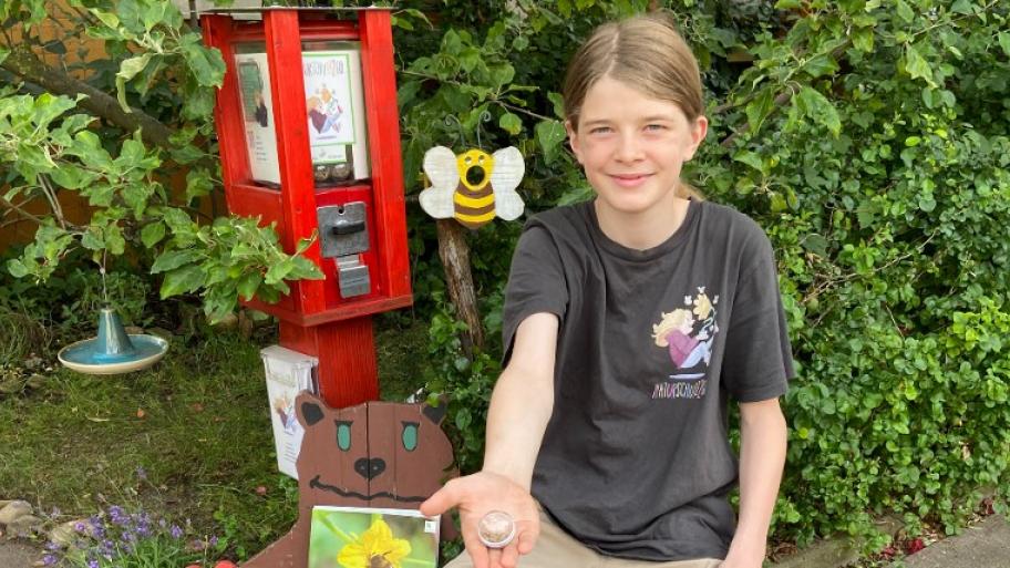 der Preisträger Jonte Mai sitzt neben einem seiner selbstgebauten Saatgutautomaten, der Automat ist rot, im Hintergrund grüne Pflanzen