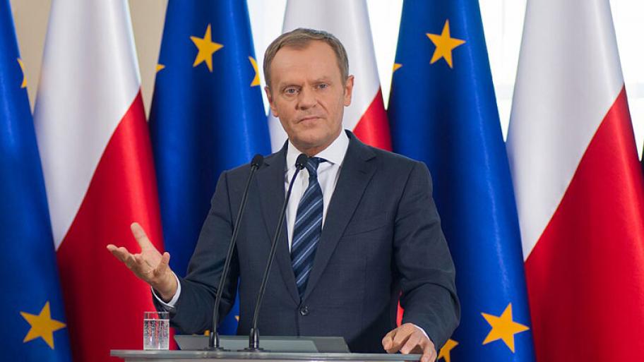 Ein Politiker im Anzug steht an einem Rednerpult, hinter ihm sind die polnische Flagge un doie EU-Fahne zu sehen