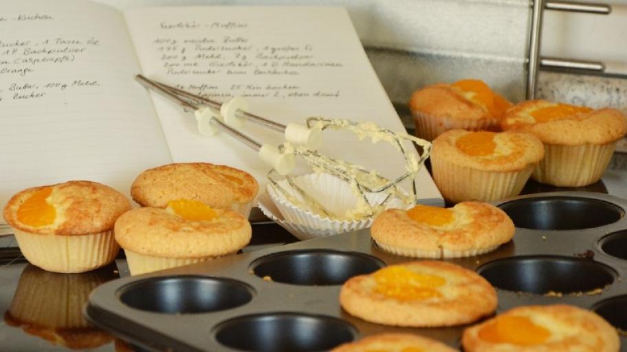 Muffinform mit gebackenen Muffins; buttrige Aufsätze eines Handmixers; Rezeptbuch