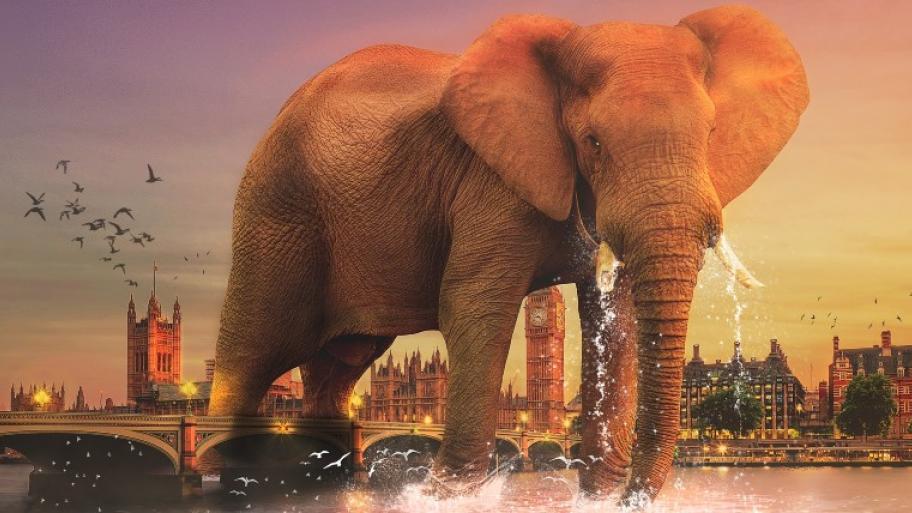 Fantasie-Bild: Elefant steht über einer Brücke in London; im Hintergrund ist die Stadt mit berühmten Sehenswürdigkeiten zu sehen, wie der Big Ben etc. 