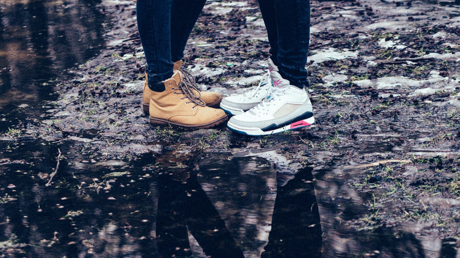 Zwei Menschen stehen dicht beieinander, Ausschnitt Schuhe und Schienbeine, im Hintergrund Weg und Pfütze
