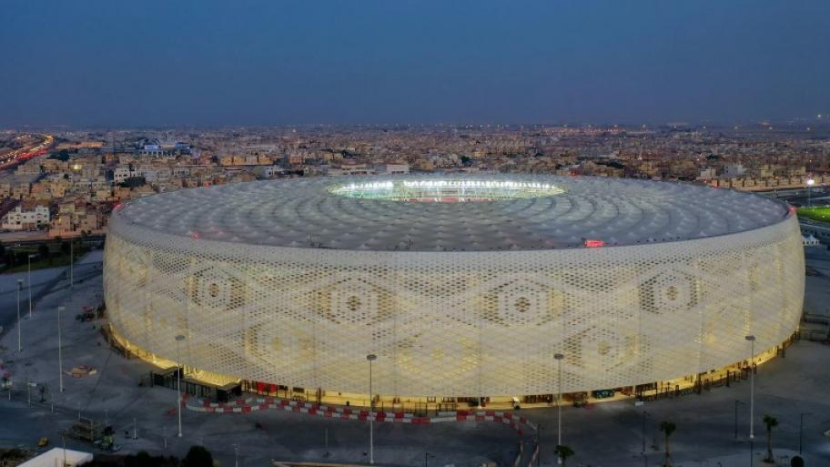 Das al-Thumama-Fußballstadion in der katarischen Hauptstadt Doha von außen in der Abenddämmerung, im Hintergrund die Stadtsilhouette von Doha 