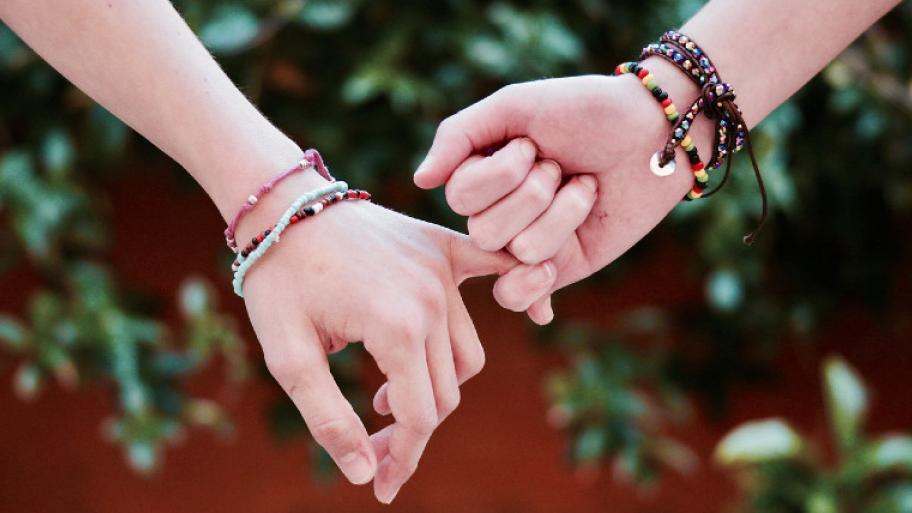 Zwei Arme mit nunten Armbändern, Personen halten sich am kleinen Finger fest, Verbundenheit, Freundschaft