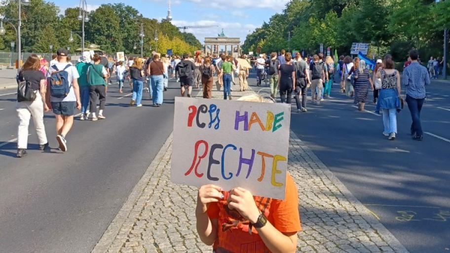 Demoplakat mit der Aufschrift: Ich habe Rechte; Kind steht auf einer Demo vor dem Brandenburger Tor in Berlin und hält Schild vor dem Gesicht