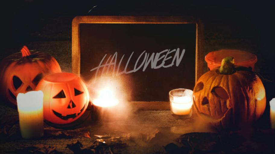 Kürbisse und Kerzen stehen neben neben einer dunklen Tafel mit dem Schriftzug "Halloween".