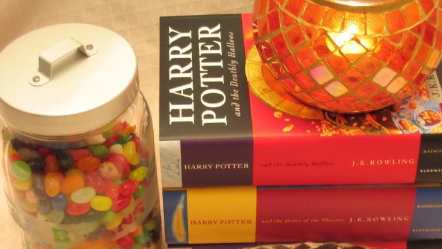 eine Auswahl von drei Harry Potter Büchern ist zu sehen. Daneben ist ein Gefäß mit Berti Botts Bohnen zu sehen. Auf dem obersten Buch ist eine Kerze zu sehen